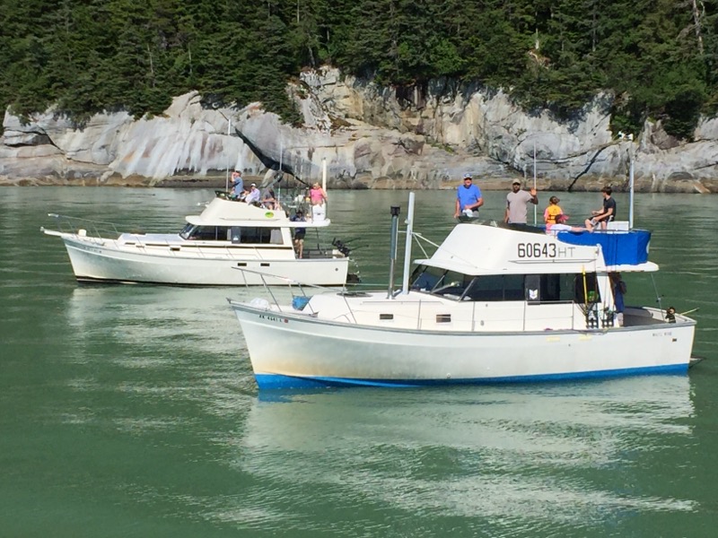 2 charter boat with lounging, smiling, waving guests in calm Alaska waters